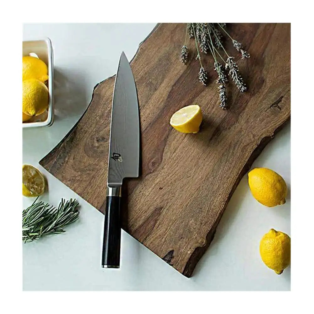 Wooden cutting board with a knife, lemons, and herbs on a light surface