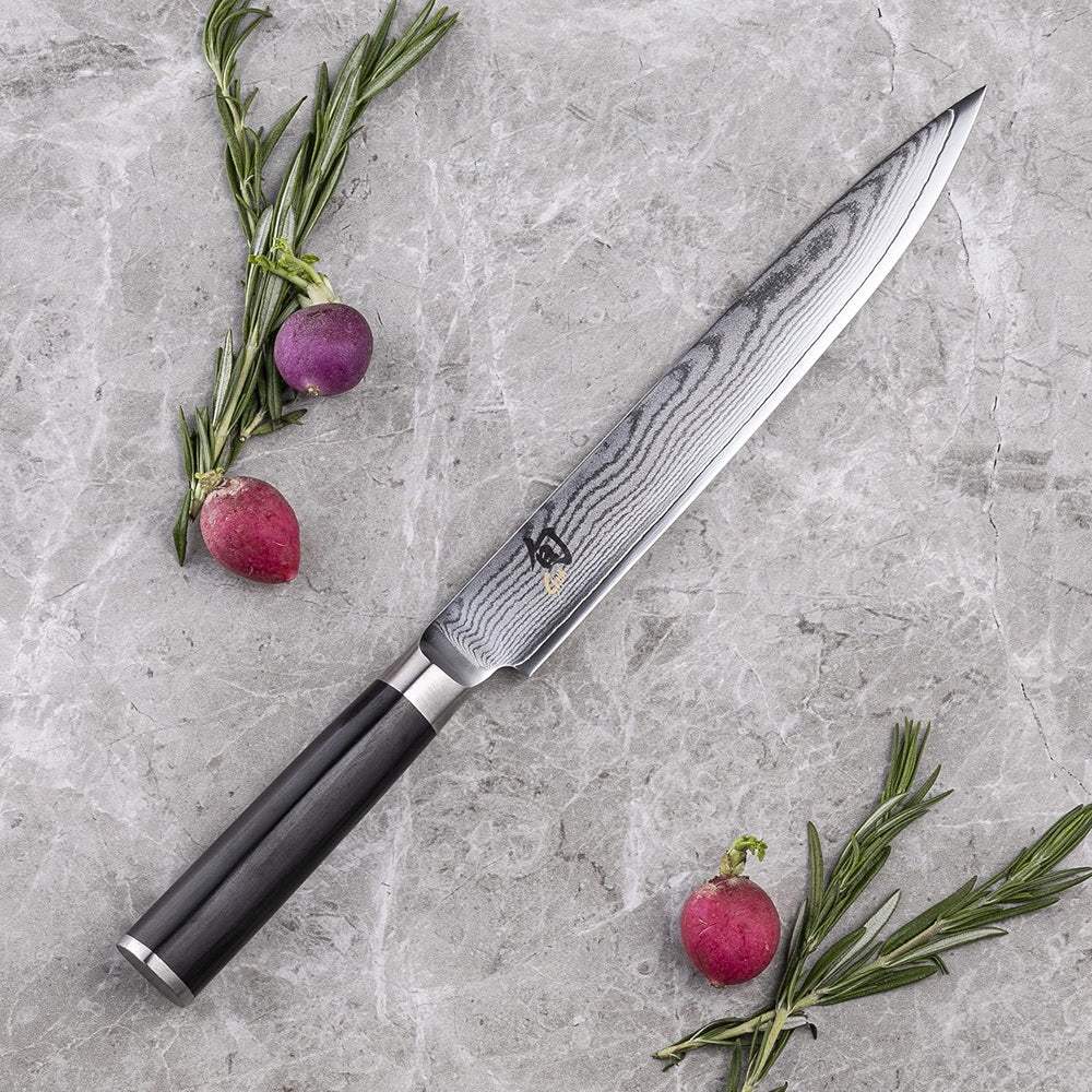 Chef's knife with a black handle on a gray surface with radishes and rosemary.