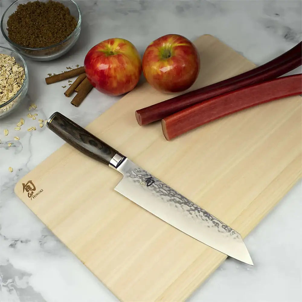 Knife on a wooden cutting board with apples, cinnamon sticks, and oats on a marble surface