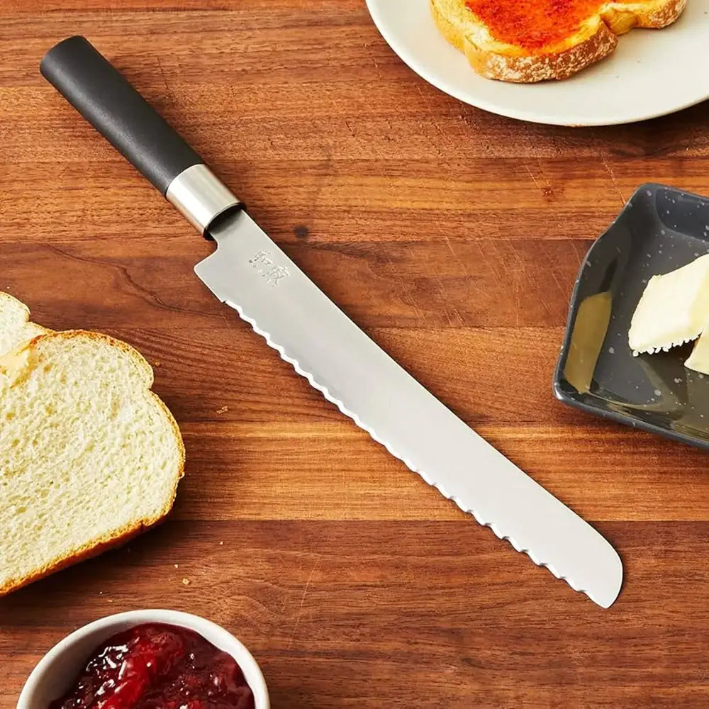 Bread knife on a wooden surface with bread, butter, and jam.