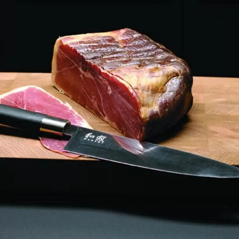 Ham and knife on a wooden cutting board with a black background