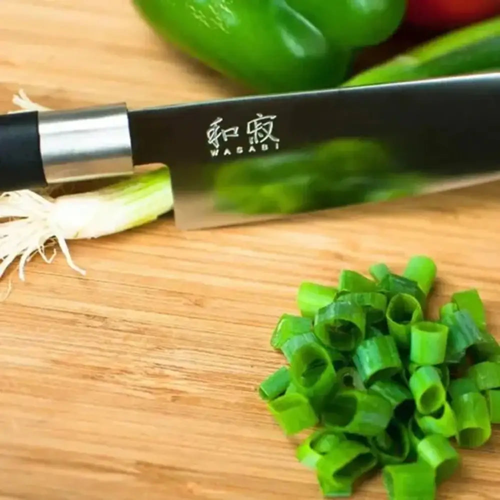 Knife with branding on a wooden cutting board with chopped green onions and vegetables.