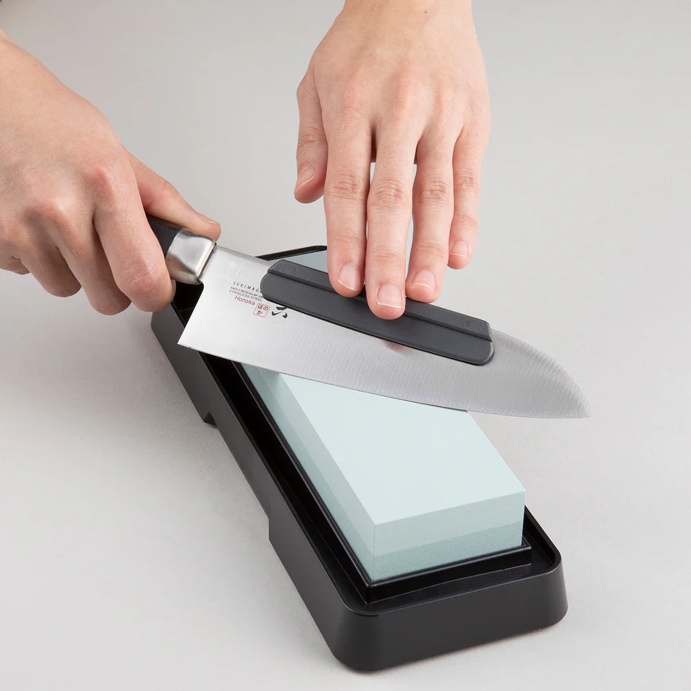 Person sharpening a knife on a whetstone with a gray background