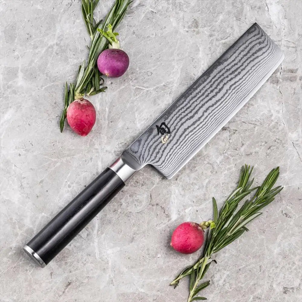 Chef's knife with a black handle on a gray surface with radishes and rosemary.