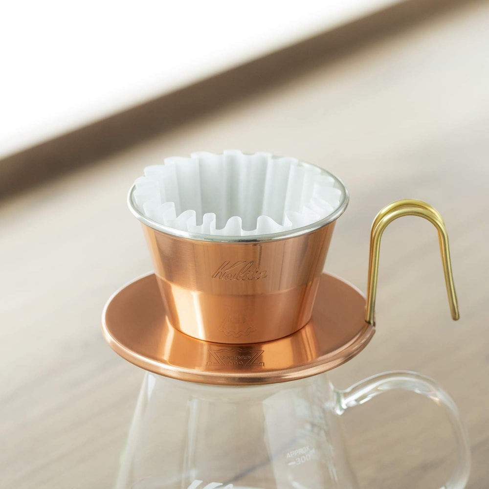 Copper coffee dripper with white filter on a beige surface