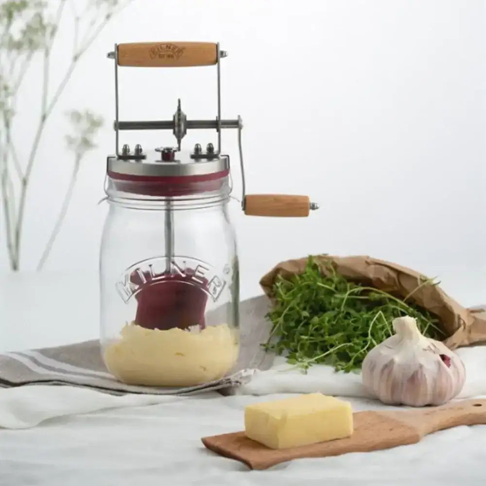Mason jar with a manual cheese press on a white surface with garlic and herbs.