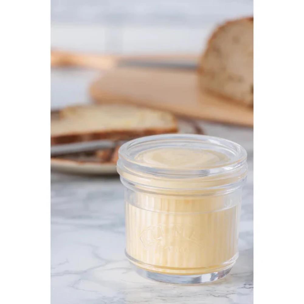 Jar of cream on a marble surface with bread in the background