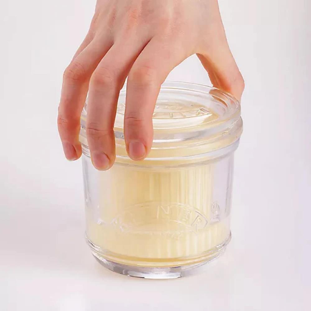 Clear glass container with lid held by a hand on a white background