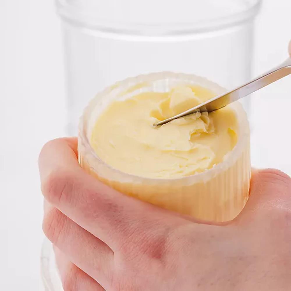 Hand holding a jar of butter with a knife