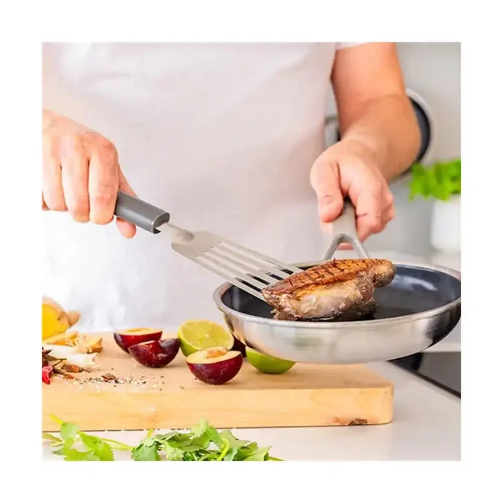 Person cooking a steak in a pan with a spatula, surrounded by fruits and vegetables on a cutting board.
