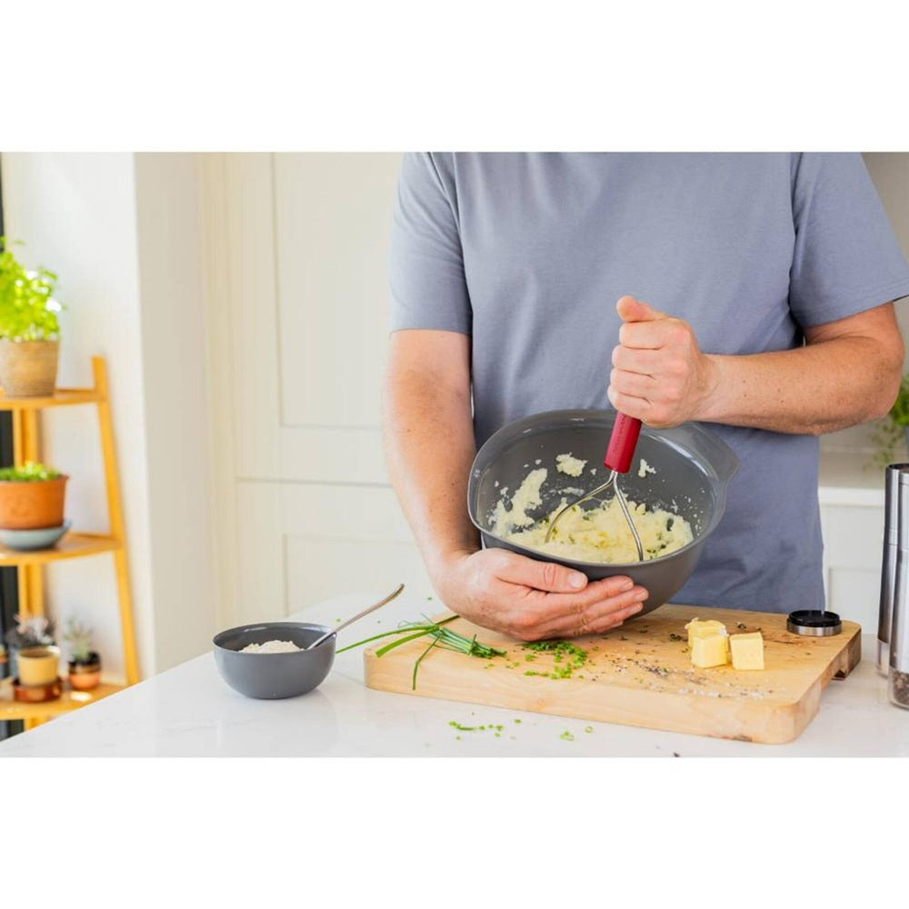 man mashing potato in a mixing bowl with a Stainless Steel wire masher with a red plastic handle on a white background