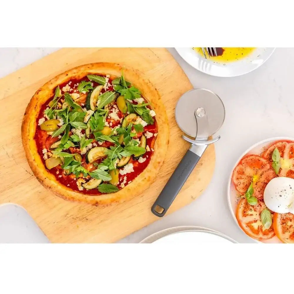 Vegetable pizza on a wooden board with a pizza cutter, served on a white plate.