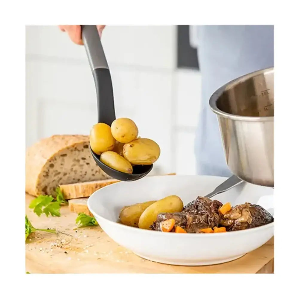 Spoon holding potatoes over a bowl of stew with bread on a wooden surface