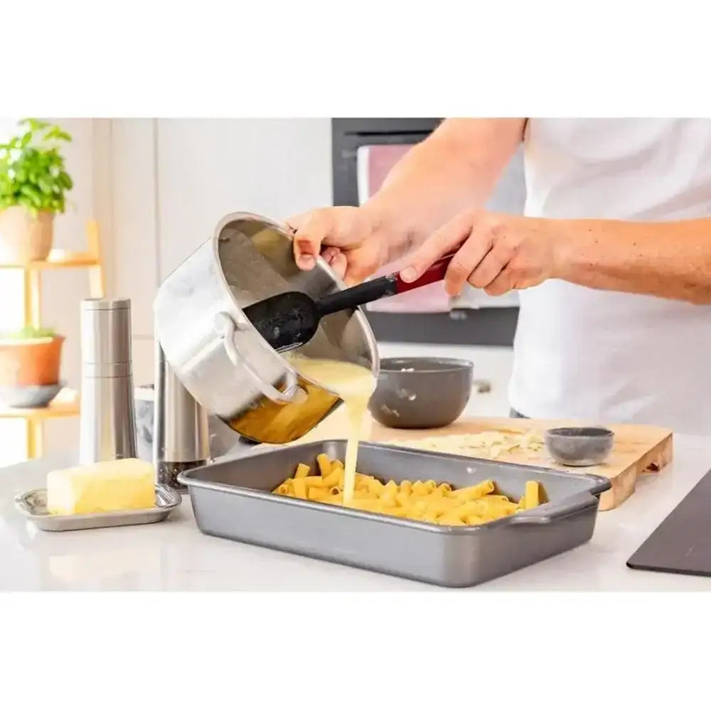 Person pouring a mixture from a pot into a baking tray in a kitchen.