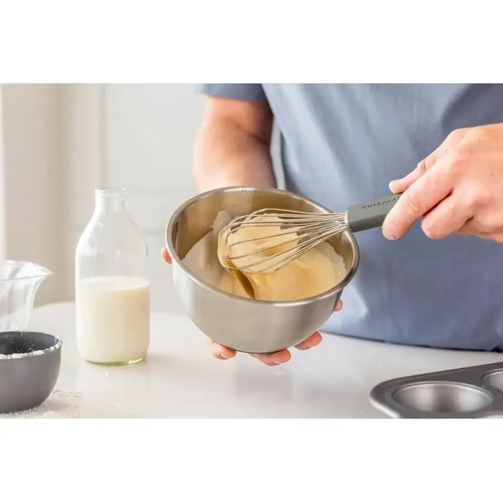 Person whisking batter in a bowl with a whisk, standing in a kitchen.