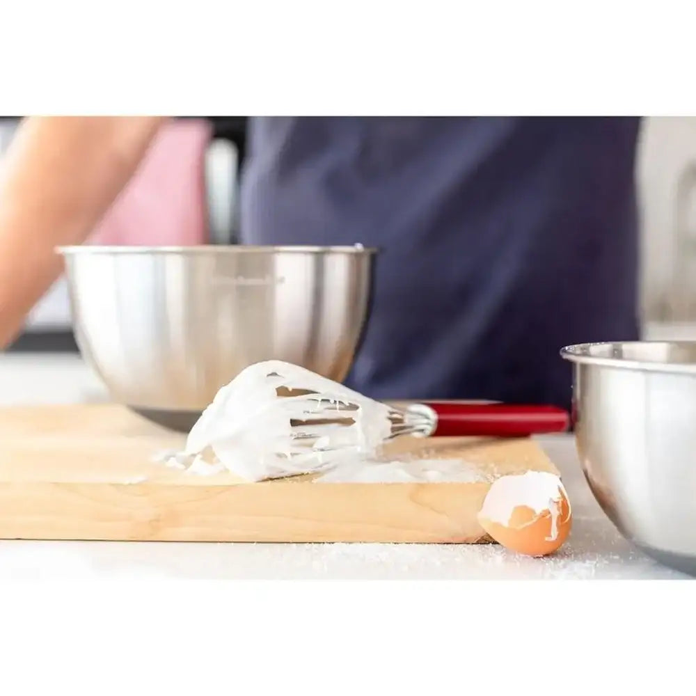 Baking setup with a whisk, rolling pin, and bowls on a white surface.