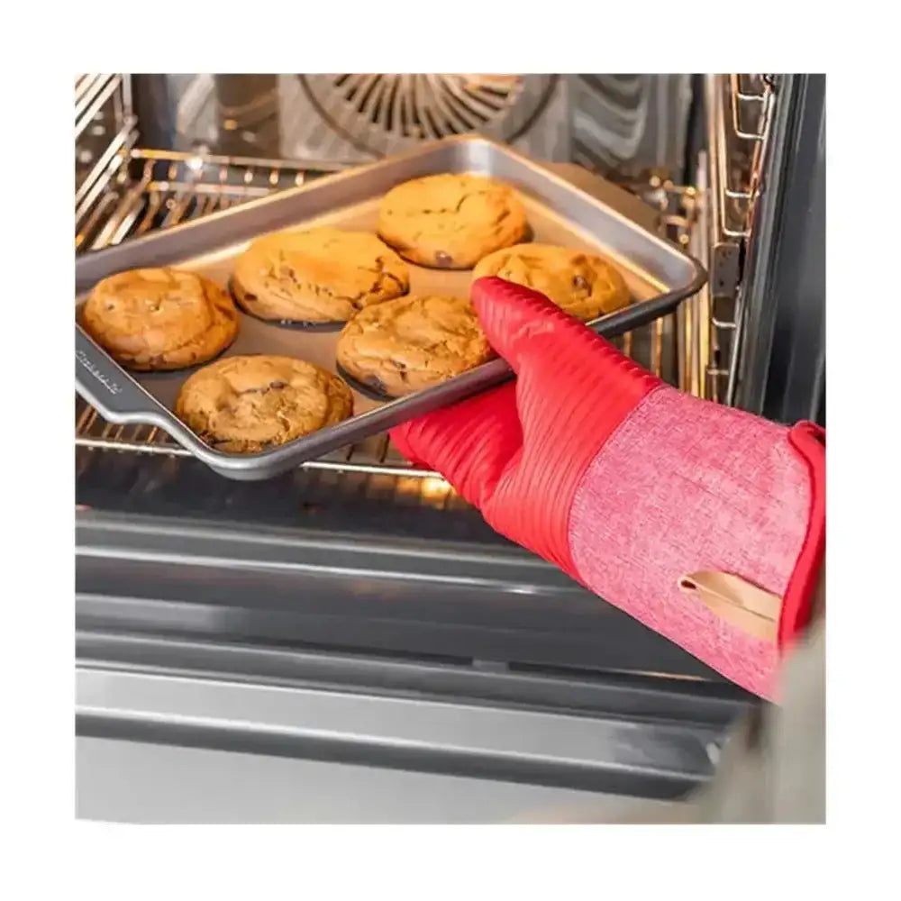 Person wearing a red oven mitt removing a tray of cookies from an oven.
