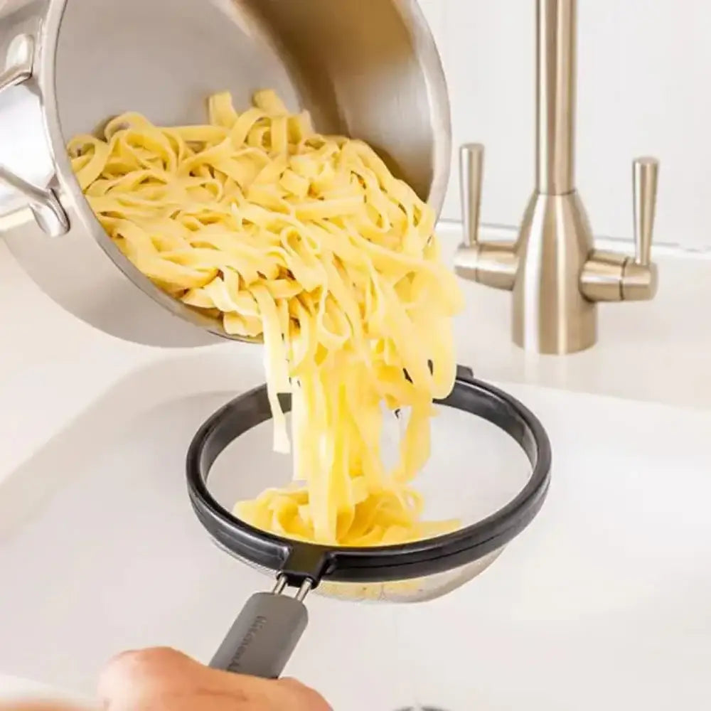 Pasta being drained from a pot into a colander over a sink.