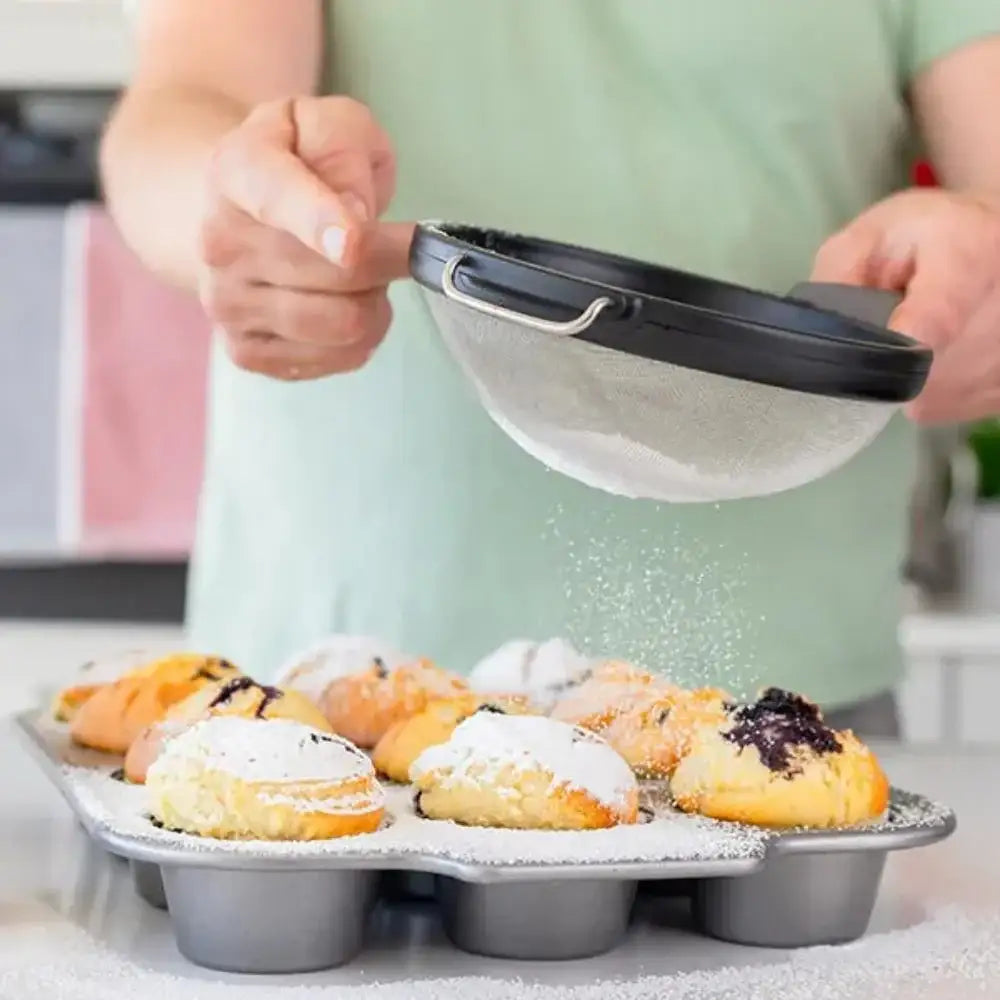 Person dusting powdered sugar over pastries using a sifter.