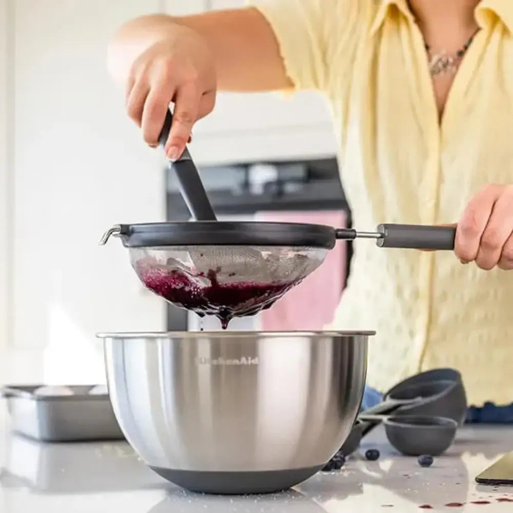 Person using a KitchenAid stand mixer with a strainer over a bowl.