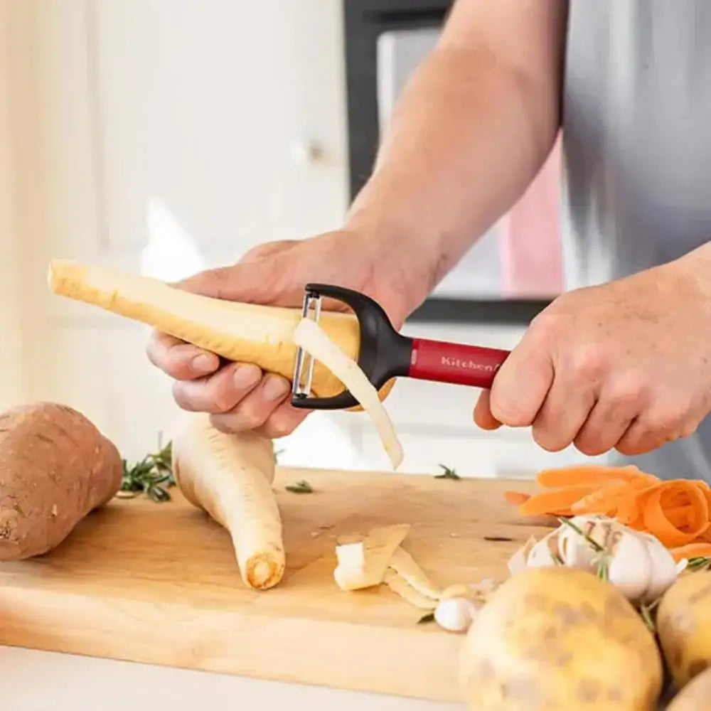 Person using a vegetable peeler on a carrot with various vegetables on a cutting board.