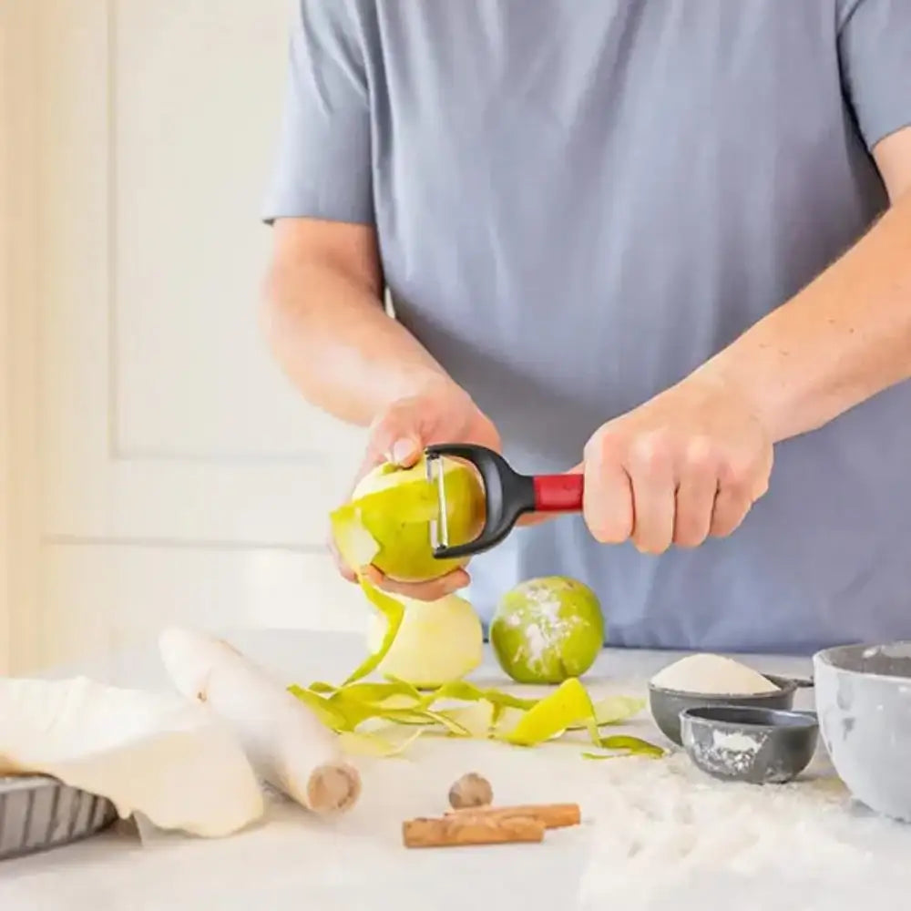 Person peeling an apple with a peeler on a kitchen counter.
