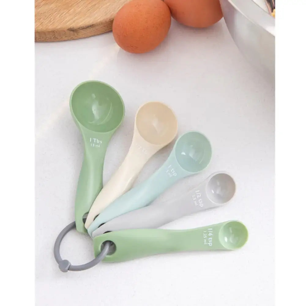 Set of measuring spoons in various colors on a white surface with eggs in the background.