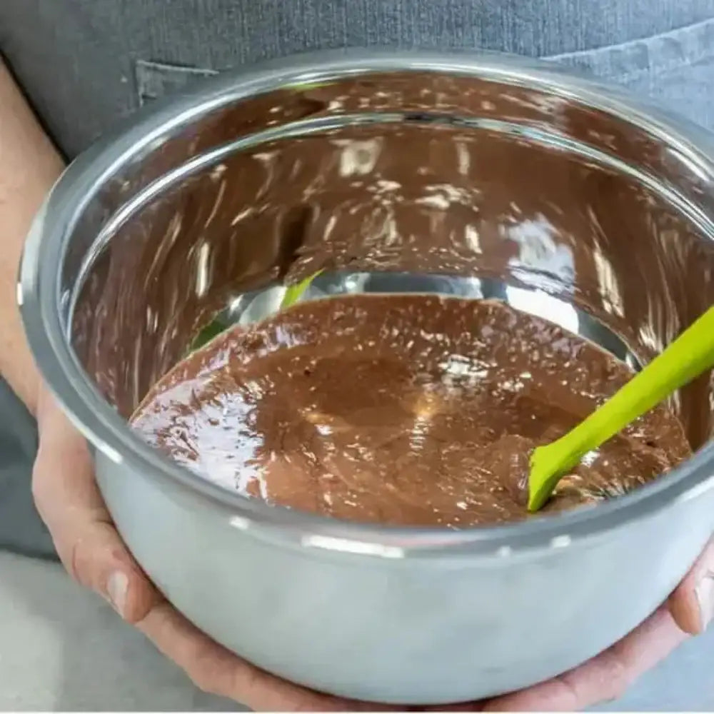 Person holding a metal bowl with chocolate mixture and a green spatula.