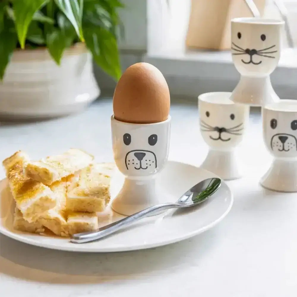 Egg in a dog-shaped egg cup on a plate with toast and a spoon, surrounded by more dog-shaped egg cups.