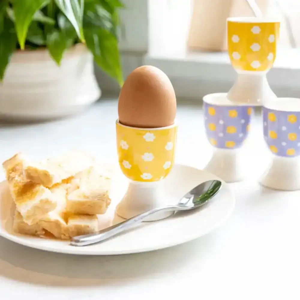 Egg in a yellow polka dot holder on a plate with bread and a spoon, with more holders in the background.