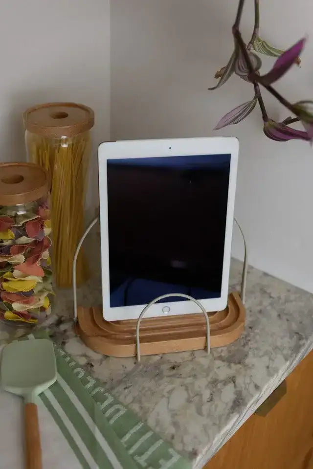 Tablet on a stand on a kitchen counter with jars and a plant in the background