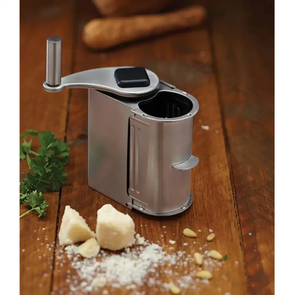 Manual cheese grater on a wooden surface with cracked pepper and herbs.