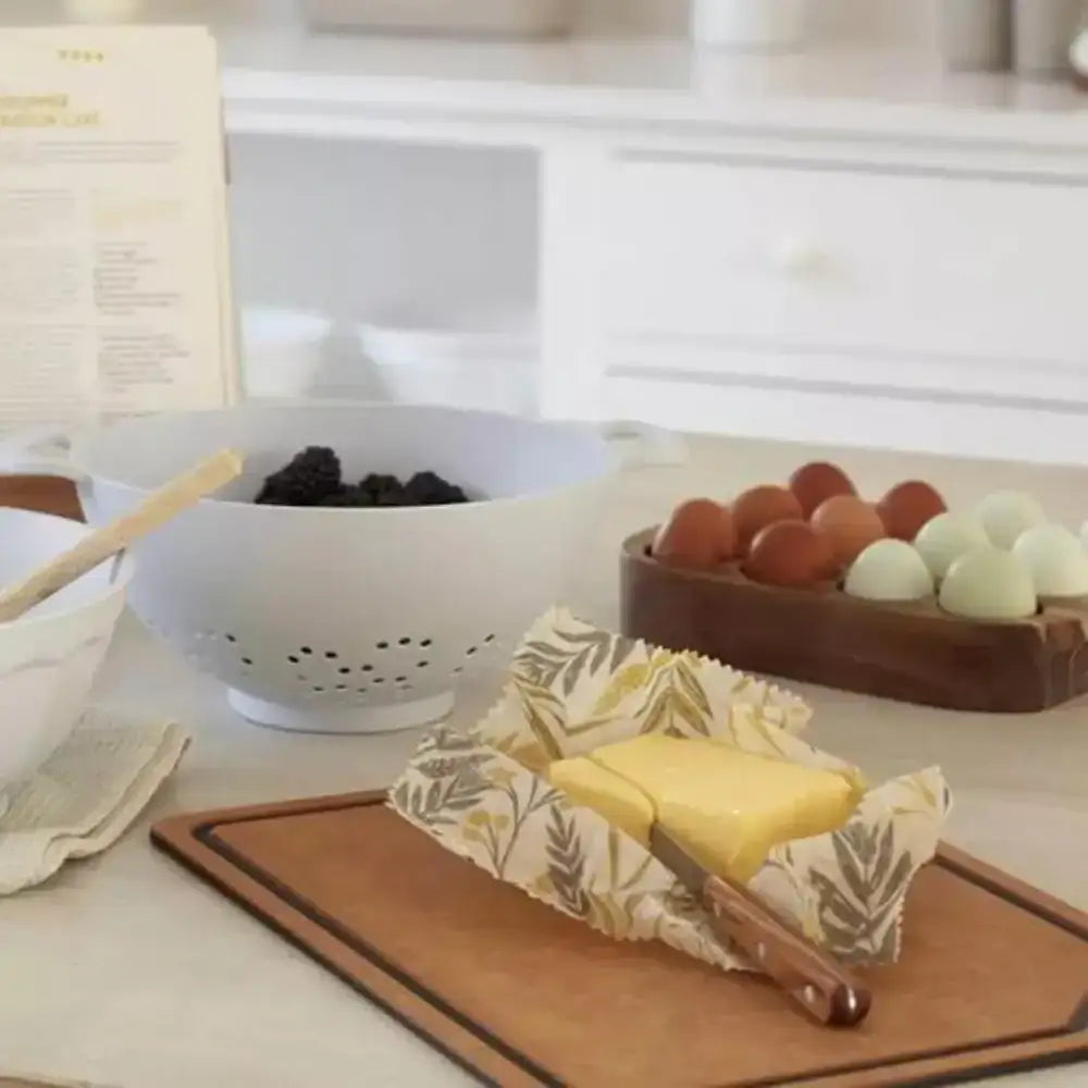 Butter on a wooden cutting board with a white colander and eggs in the background.