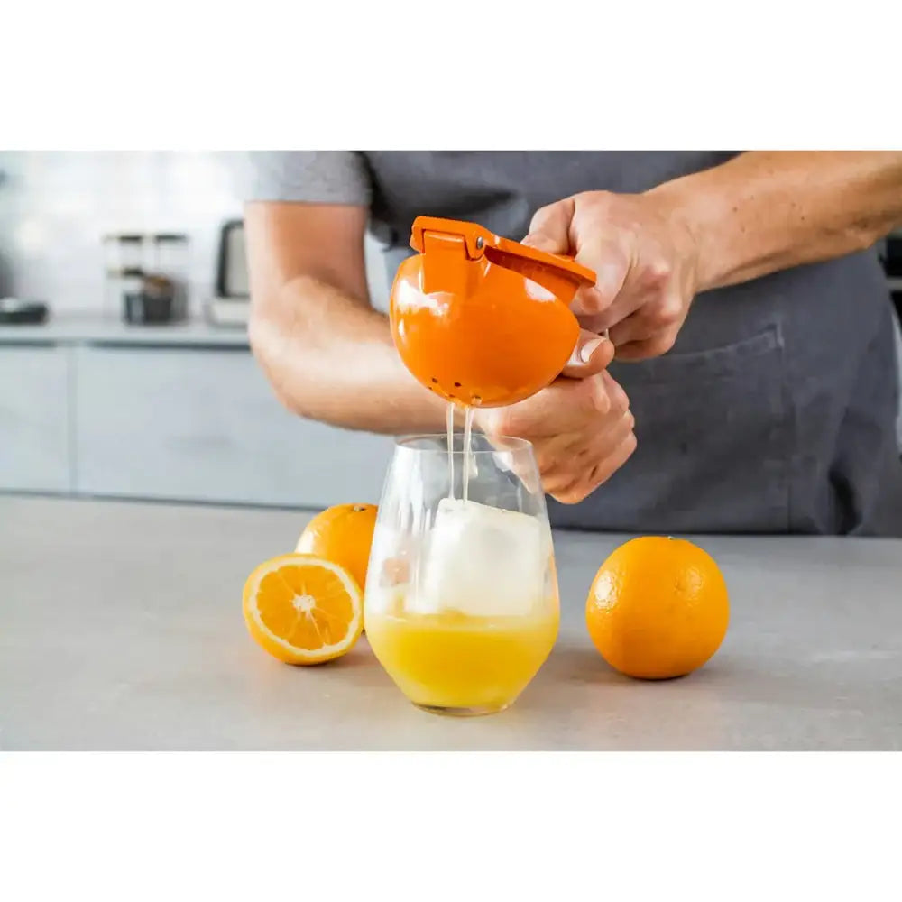 Person using a manual juicer to extract juice from an orange, with a glass of orange juice on a kitchen counter.