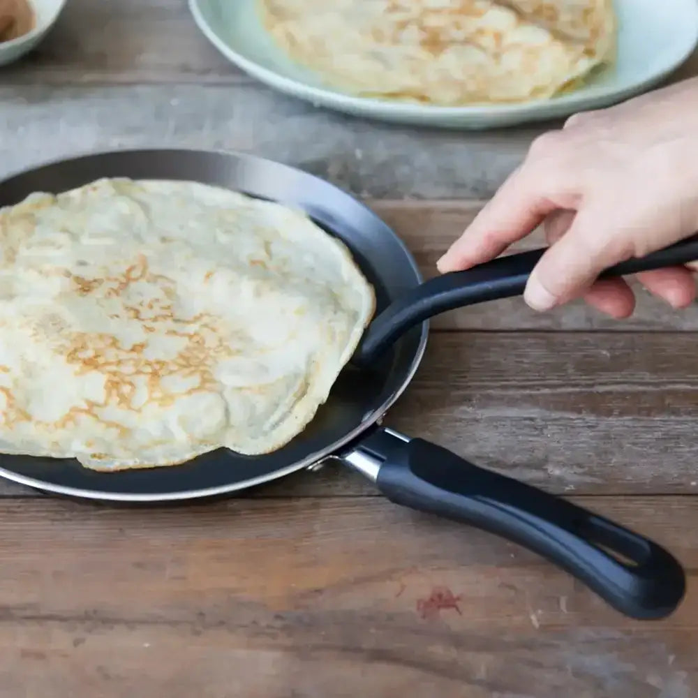 Person flipping a crepe on a pan with a wooden background