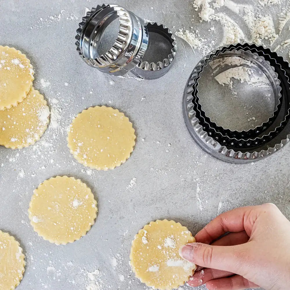 Hand shaping cookie dough next to metal cookie cutters on a floured surface