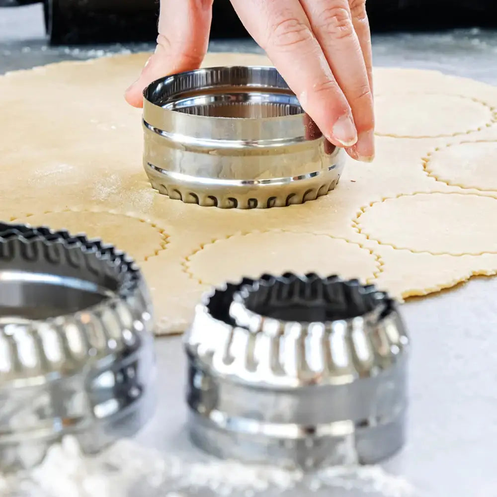 Metallic pie crust cutters being used on rolled-out dough