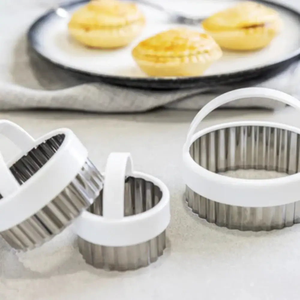 Set of metal ring cookie cutters on a white surface with pastries in the background.