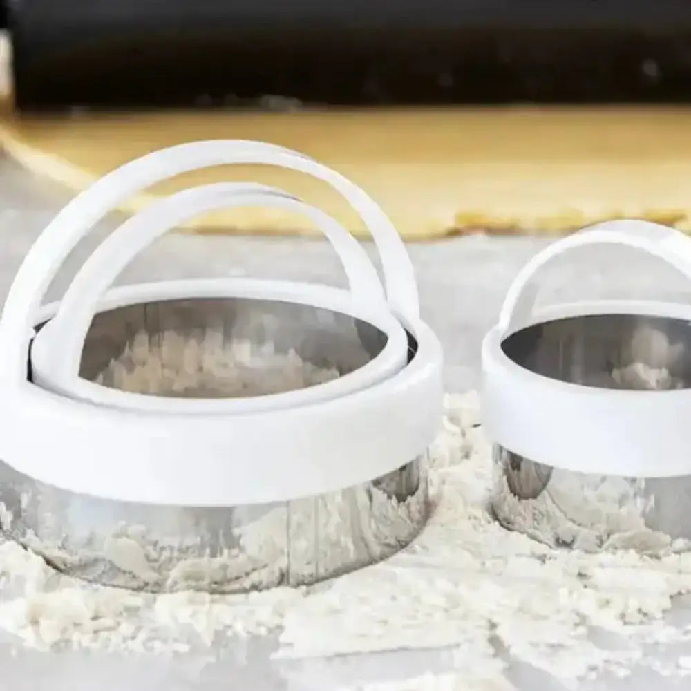 Two white metal dough cutters on a surface with flour