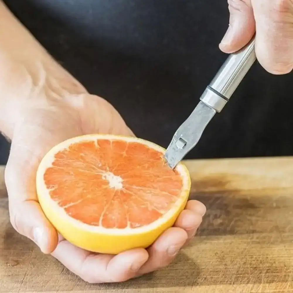 Person cutting a grapefruit with a knife on a wooden surface