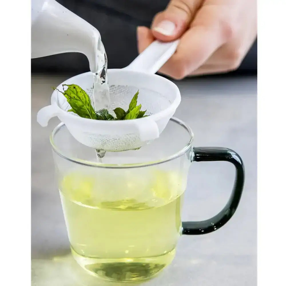Person pouring liquid into a glass mug with a mint leaf strainer.
