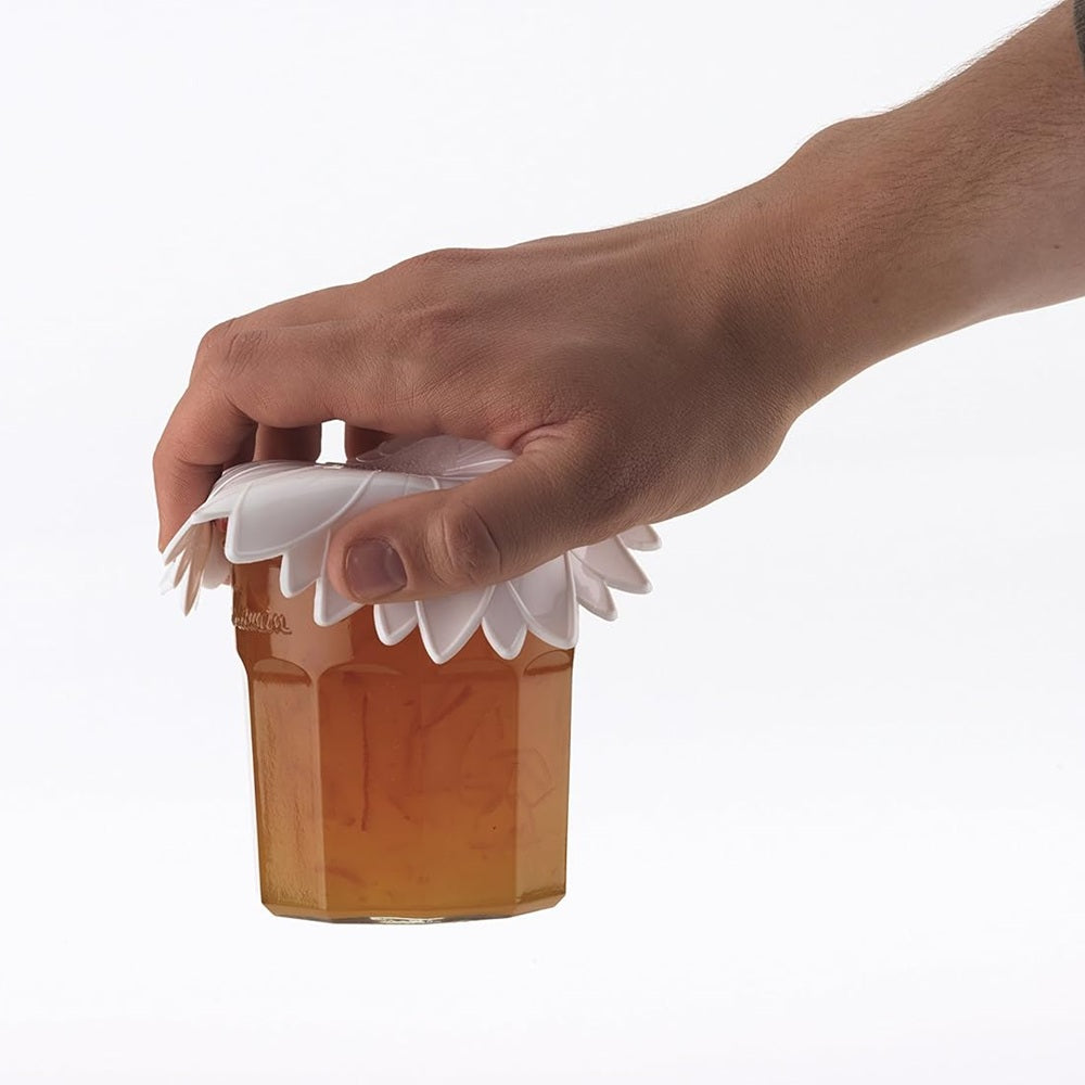 Hand holding a glass of amber liquid with a white floral lid against a white background
