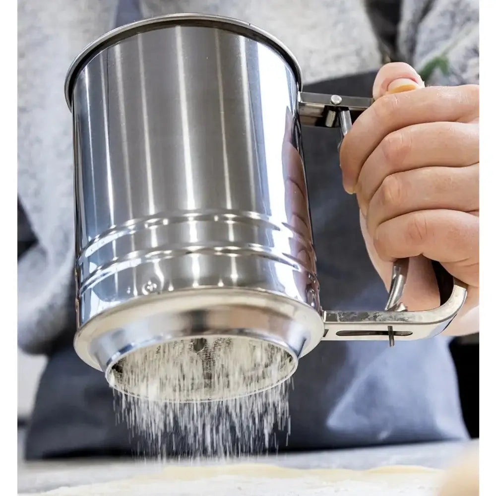 Person using a metal flour sifter to sift flour into a bowl.
