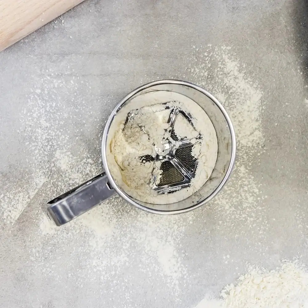 Metal sifter with flour on a gray surface