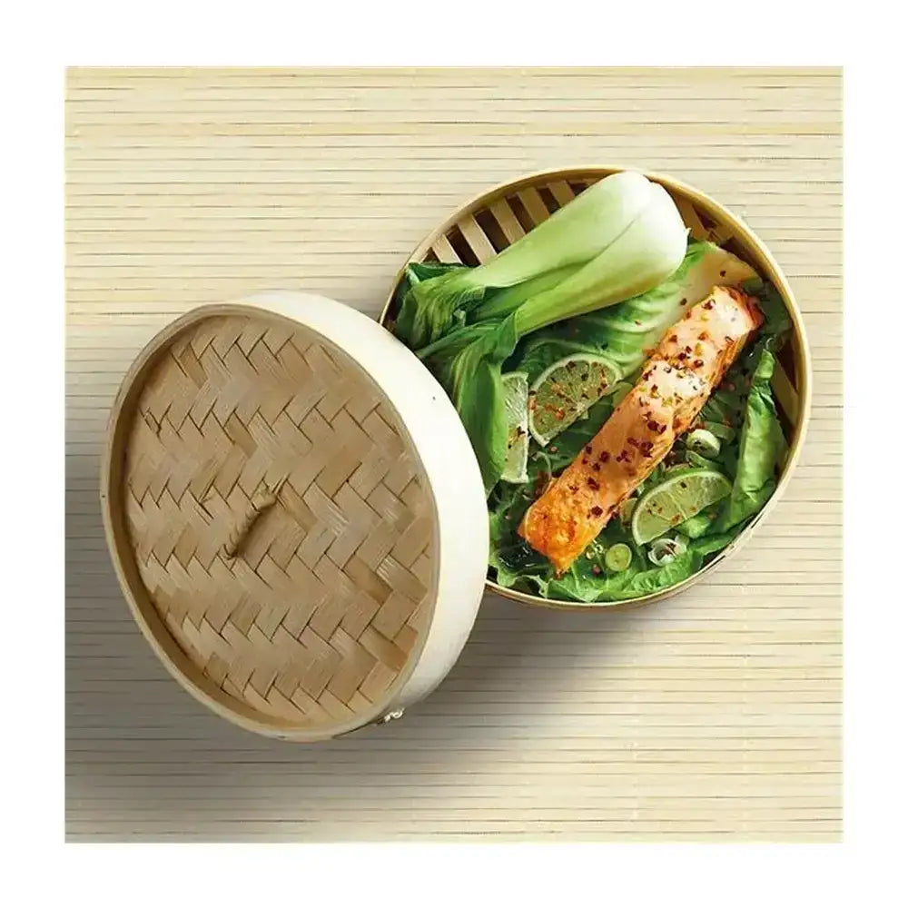 Bamboo steamer basket with salmon and greens on a wooden surface