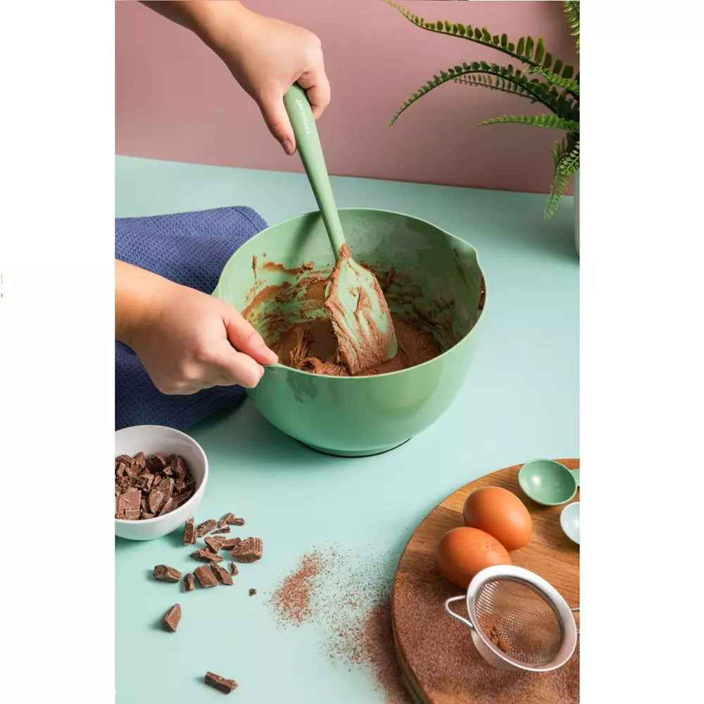 Person mixing ingredients in a green bowl with a spatula on a light blue surface.