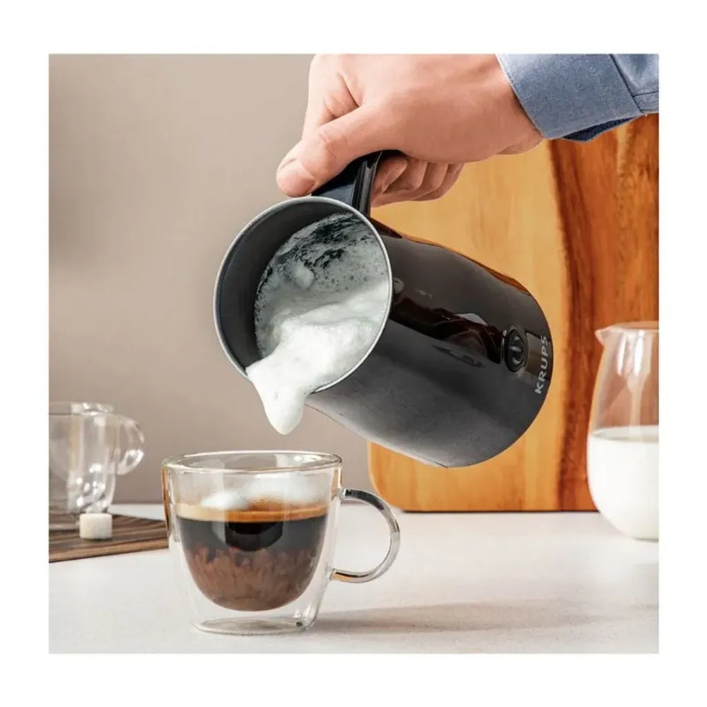 Person pouring frothed milk from a Krups milk frother into a glass of coffee.