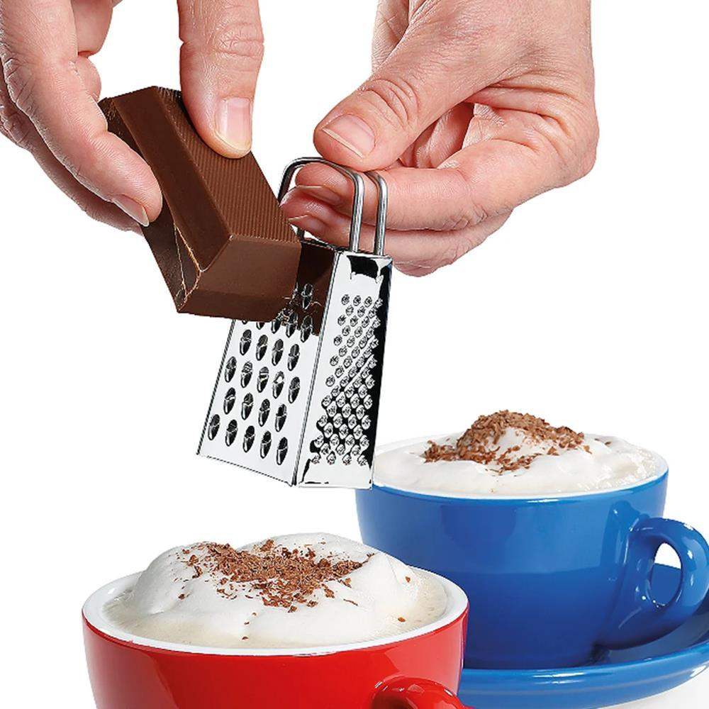 Hand using a small grater to sprinkle chocolate shavings over two cups of hot chocolate.