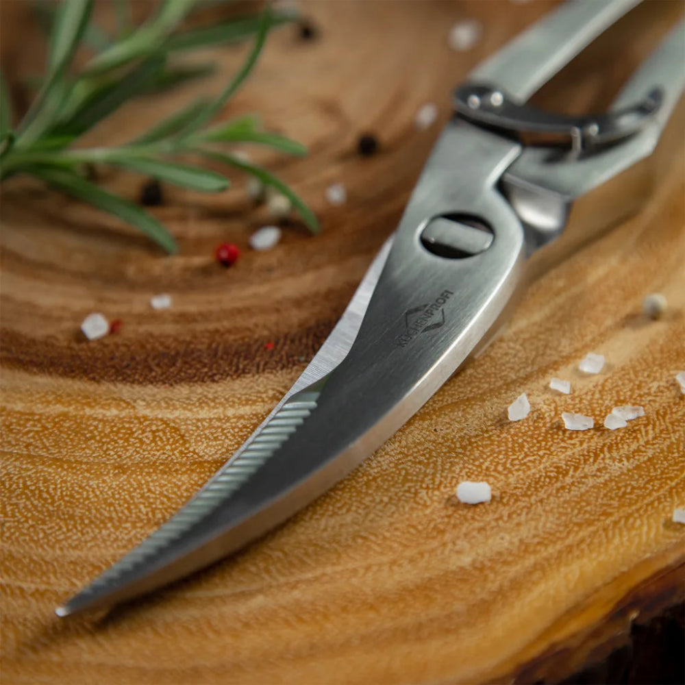 Metallic kitchen shears on a wooden surface with herbs and spices.