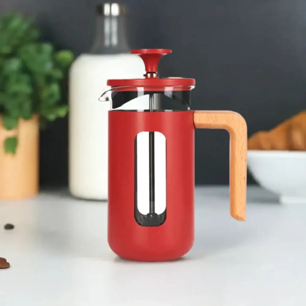 Red French press coffee maker with wooden handle on a white surface.